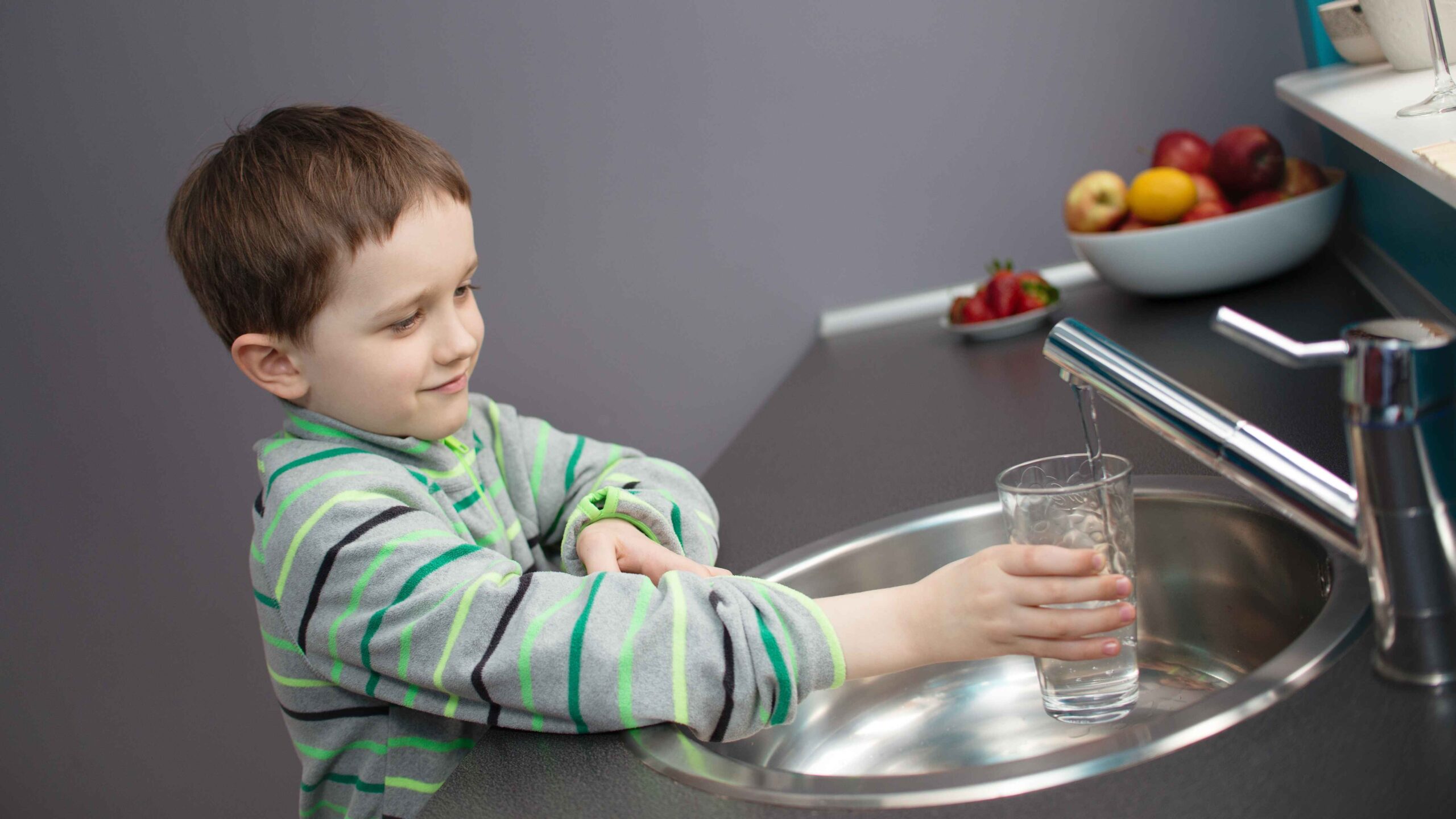 Child filling a glass with water from a kitchen tap, representing EcoWater's alkaline treatment and remineralization process